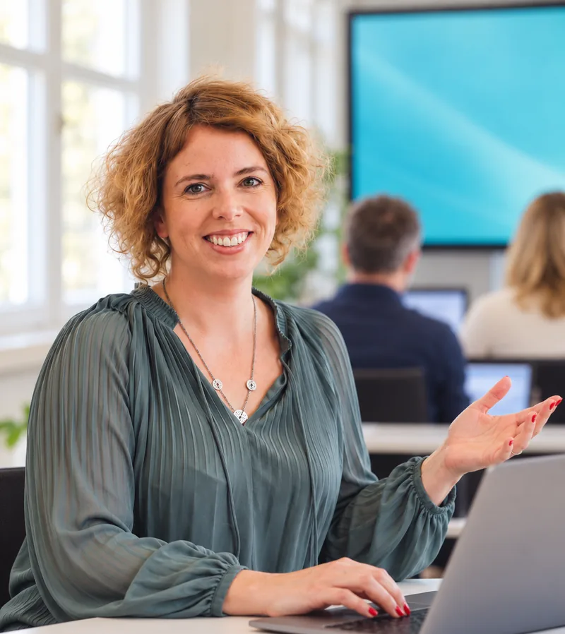 Stefanie Gründler sitzt im Kursraum am Laptop, dahinter Teilnehmende an ihren Laptops